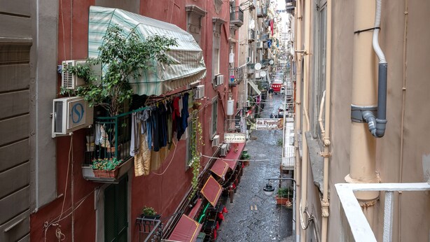 A narrow street with buildings on either side, some with balconies and outdoor seating areas. - arbiter toledo - 2 apartments (Napoli)