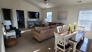 A living room with a sofa, dining table, chairs, a TV, and a ceiling fan. - Pet Friendly Home with Private Tiki Bar - 3-minute drive to the beach! (Kill Devil Hills)
