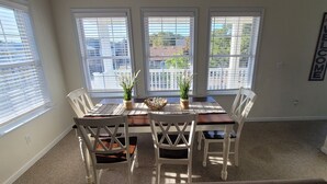 A dining area with a table and chairs, large windows with blinds, and a 'WELCOME' sign on the wall. - Pet Friendly Home with Private Tiki Bar - 3-minute drive to the beach! (Kill Devil Hills)