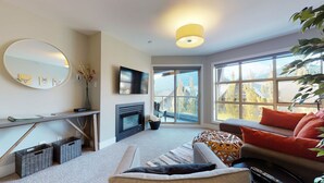 Una sala de estar moderna con chimenea, un televisor de pantalla plana, un ventanal con vistas a la montaña y una zona de estar acogedora.