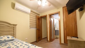 A bedroom with a bed, an air conditioner, a ceiling fan, wooden doors, and a television on a stand.