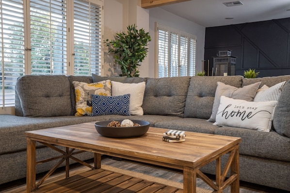 Una sala de estar moderna con un sofá seccional gris, una mesa de centro de madera y cojines decorativos.