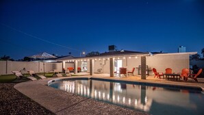 Un área de piscina moderna al aire libre con sillones de descanso, una parrilla y un porche cubierto.