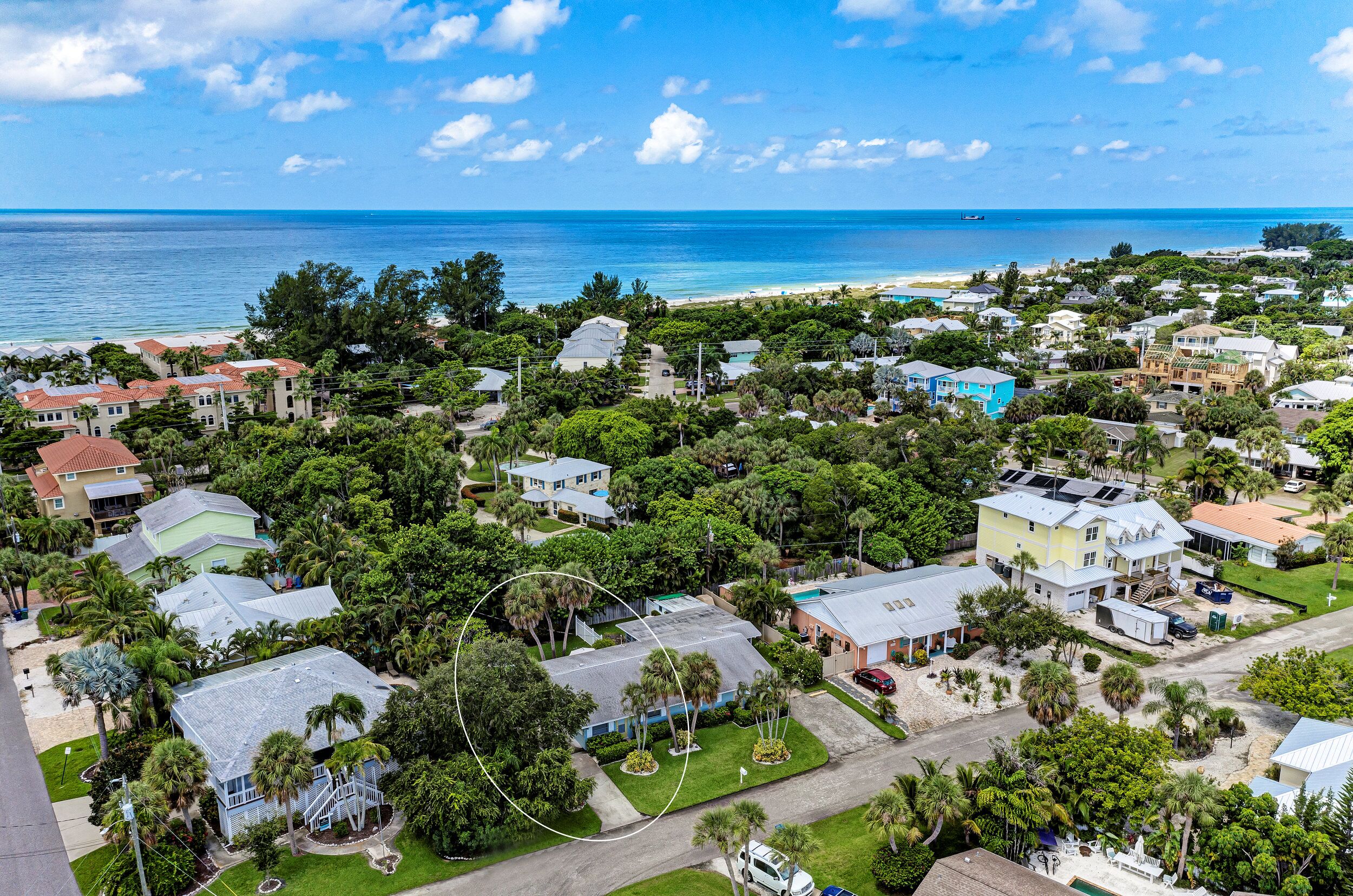 Vue aérienne d’un quartier résidentiel situé sur la côte, avec des maisons, des palmiers et une plage.