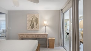 A bedroom with a bed, a desk, a lamp, a wicker basket, and a sliding glass door leading to a dining area.
