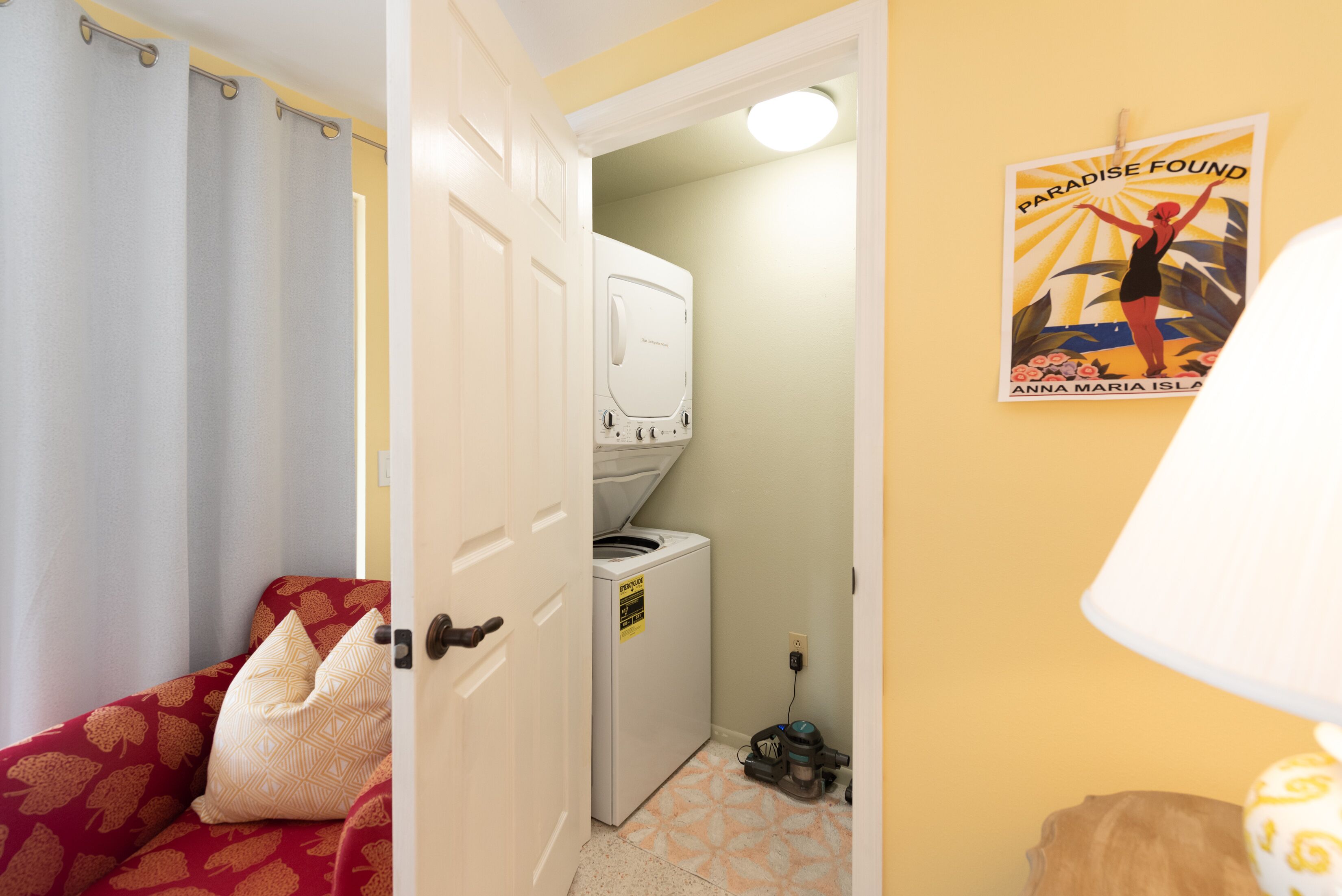 A compact room with a washing machine, a bed with patterned bedding, and a poster on the wall.
