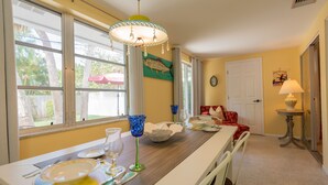 A dining area with a wooden table set for a meal, a chandelier, and a view of the outdoors through large windows.