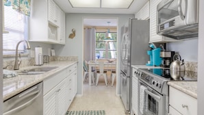 A modern kitchen with white cabinetry, stainless steel appliances, and a dining area with white chairs and a table.