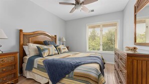 A bedroom with a wooden bed, a ceiling fan, a window with blinds, and a dresser.