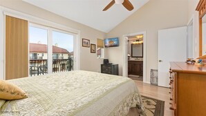 A bedroom with a large bed, a ceiling fan, a TV, and a view of the outside balcony.