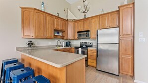 A kitchen with wooden cabinets, a stainless steel refrigerator, a microwave, and a stove. There are blue stools and a large island.