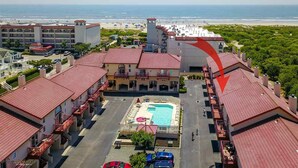 A hotel with a central swimming pool, multiple balconies, and a view of the beach and ocean.