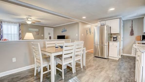 Una cocina moderna con armarios blancos, un refrigerador de acero inoxidable y un comedor con una mesa de madera y sillas blancas.