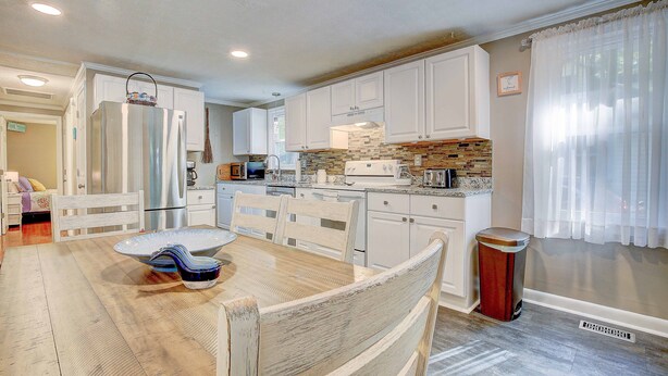 Una cocina moderna con armarios blancos, una isla central y una zona de comedor con sillas de madera.