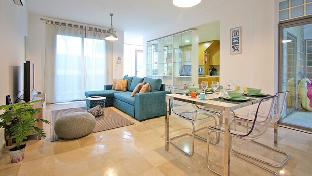 A modern living room with a sofa, dining table, and chairs. There is a television, a potted plant, and a window with curtains. - Believe in Dream, Apart. Contemporâneo com Piscina (Tavira - Santa Maria)