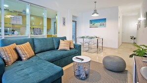 A modern living room with a sectional sofa, a dining area with a glass table, and a kitchen visible through a glass partition. - Believe in Dream, Apart. Contemporâneo com Piscina (Tavira - Santa Maria)