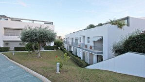 A modern residential building with a flat roof, large windows, and a small garden area with a tree and shrubs. - Believe in Dream, Apart. Contemporâneo com Piscina (Tavira - Santa Maria)