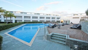 A swimming pool with lounge chairs and a wooden deck, surrounded by a modern building with multiple balconies. - Believe in Dream, Apart. Contemporâneo com Piscina (Tavira - Santa Maria)