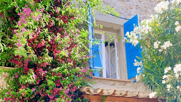 A stone building with a balcony, a white door, and blue shutters.