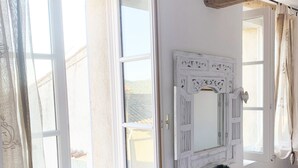 A room with a white vanity, a large mirror, and a window with curtains.