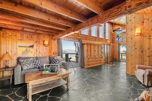 Interior de madeira com piso de pedra, um sofá, uma mesa de centro e vista para o exterior.