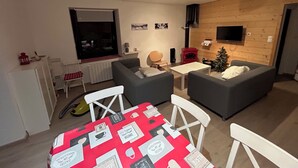 Un salon chaleureux avec deux canapés gris, une petite table blanche et une nappe rouge ornée de diverses cartes.
