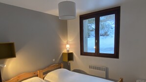 Une chambre avec deux lits simples, une table de chevet avec une lampe, une fenêtre donnant sur un paysage enneigé et un radiateur.