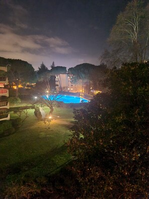 Vista nocturna de una piscina rodeada de árboles y edificios.