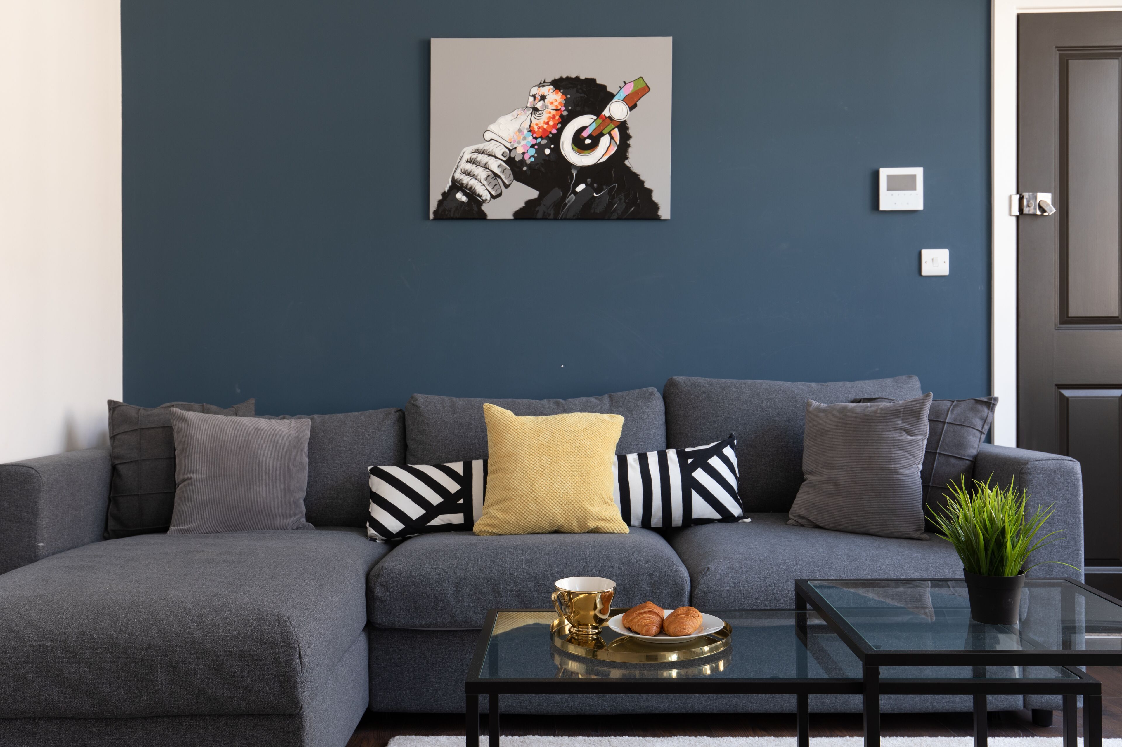 Un salon moderne avec un canapé gris, une table basse en verre et un tableau accroché au mur.