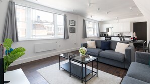 A modern living room with a grey sofa, a glass coffee table, and a view of the city through large windows. - home.ly London Liverpool Str Apartments (London)