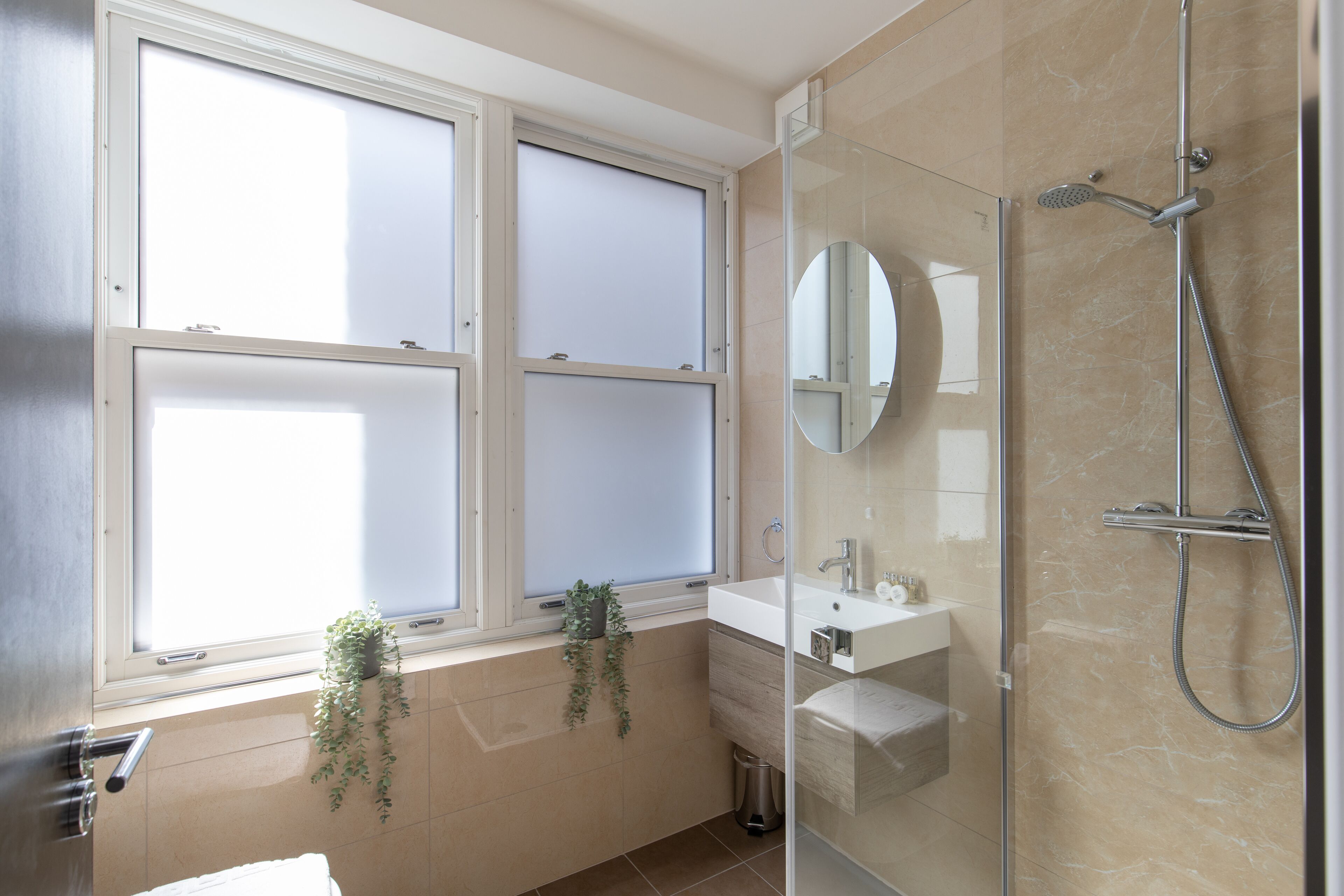 A modern bathroom with a glass shower enclosure, a white sink, and a window with frosted glass.