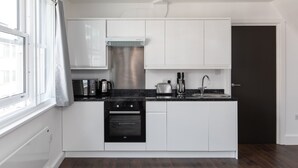 A modern kitchen with white cabinets, a black countertop, stainless steel appliances, and a window with curtains. - home.ly London Liverpool Str Apartments (London)