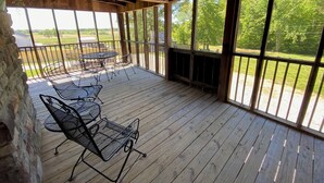 A wooden deck with metal chairs and a table, overlooking a grassy area.