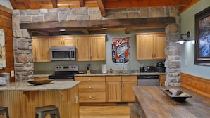 A rustic kitchen with stone walls, wooden cabinets, a granite countertop, and a bar area with stools.