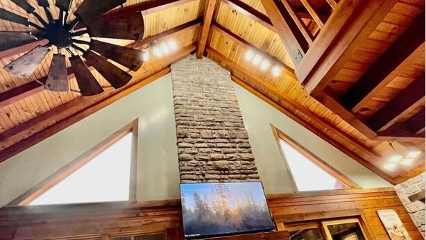 A high-ceilinged room with a stone fireplace, wooden beams, and a large window.