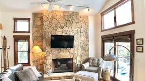 Un salón acogedor con chimenea de piedra, sofás de cuero y un televisor de pantalla plana montado encima.