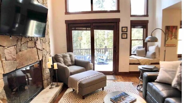 Una sala de estar amplia con chimenea de piedra, sofás de cuero, un televisor de pantalla plana y grandes ventanales con vistas al exterior.