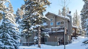 Una cabaña de varios pisos con balcón, rodeada de árboles cubiertos de nieve.