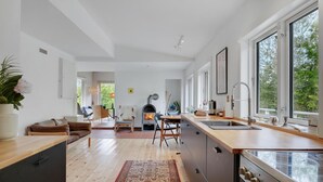 A modern kitchen with a wood-burning stove, large windows, and a view of greenery outside.