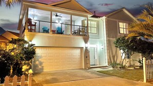 A two-story house with a garage, a balcony with a railing, and a well-lit entrance. - Beachside home/4 Kings/Pool/Pet Friendly/Sleeps 24 (Miramar Beach)