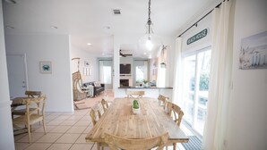 A spacious dining area with a wooden table and chairs, a hanging light fixture, and a view of the beach through a large window. - Beachside home/4 Kings/Pool/Pet Friendly/Sleeps 24 (Miramar Beach)