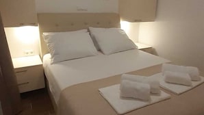 Een opgemaakt bed met witte lakens en kussens, een bedlampje en een wanddecoratie.