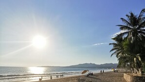 A beach with a clear sky, sun, and palm trees.