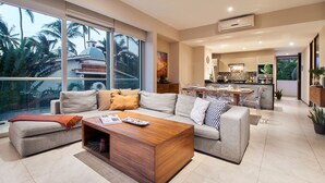 A modern living room with a sofa set, a coffee table, and a view of a kitchen and dining area.