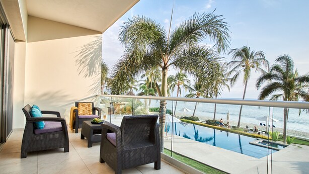 A balcony with wicker furniture, a pool, and palm trees. - Azul Bucerias 3 Brdm Beachfront,  paradise to enjoy (Bucerías)