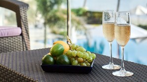 A wicker table with a fruit bowl and two glasses of champagne, overlooking a pool and palm trees.
