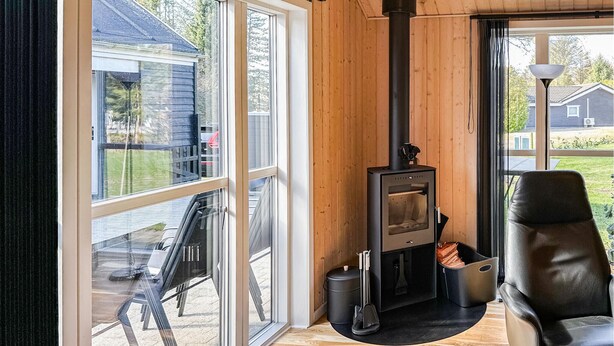 A modern interior with a wood-burning stove, a glass door leading outside, and a leather chair. - Cozy home in Løgstør with kitchen (Løgstør)