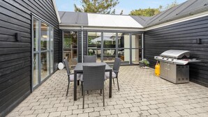 A patio with a table and chairs, a grill, and a glass-enclosed area with furniture. - Cozy home in Løgstør with kitchen (Løgstør)