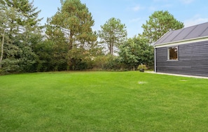 A residential property with a well-maintained lawn, a dark wooden house, and surrounding trees.