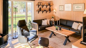 A modern living room with a sofa, armchair, and coffee table, wooden floors, and a large window with a view of a garden. - Cozy home in Løgstør with kitchen (Løgstør)